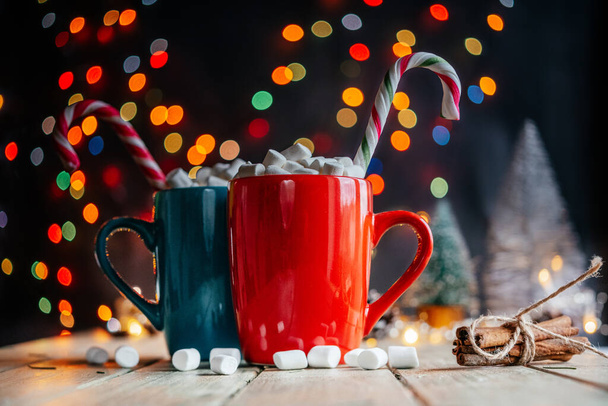Красный и зеленый чашки горячего шоколада с зефиром и конфеты трости на рождественском фоне - Фото, изображение