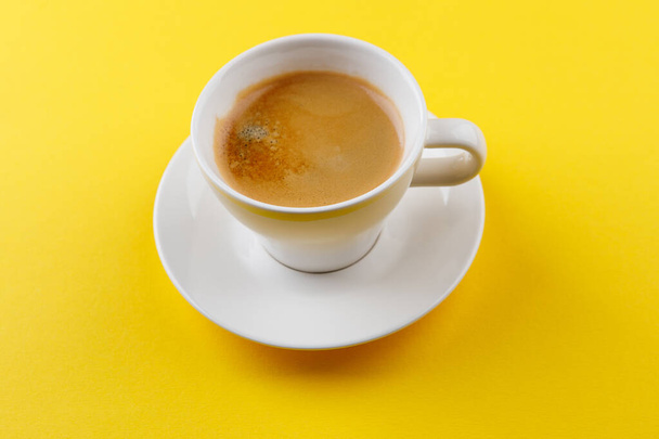 Black coffee in a cup on a yellow background - Fotoğraf, Görsel