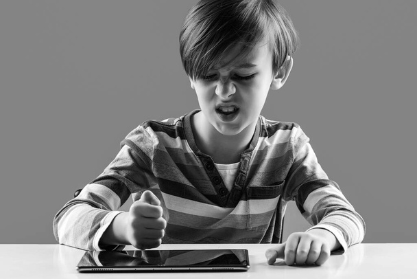 Nervous boy studying online with laptop. Upset child has problem with gadget. Negative emotions during online lesson. Education, online learning and gaming at home. Angry boy hitting his tablet. - Photo, Image