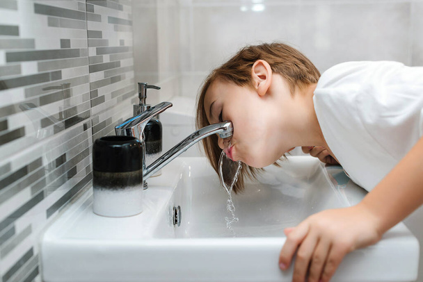 Chlapec myje obličej v koupelně. Ranní hygiena. Mladý chlapec je umytý v umyvadle. Zdravé dětství a životní styl. Zubní hygiena každý den. Zdravotní péče, dětská a zubní hygiena. - Fotografie, Obrázek