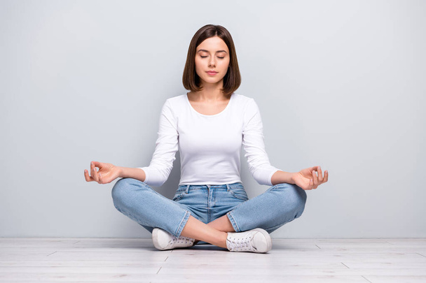 Photo of dreamy peaceful young woman wear white outfit sitting legs crossed practicing yoga smiling isolated concrete grey wall background - Foto, Imagem