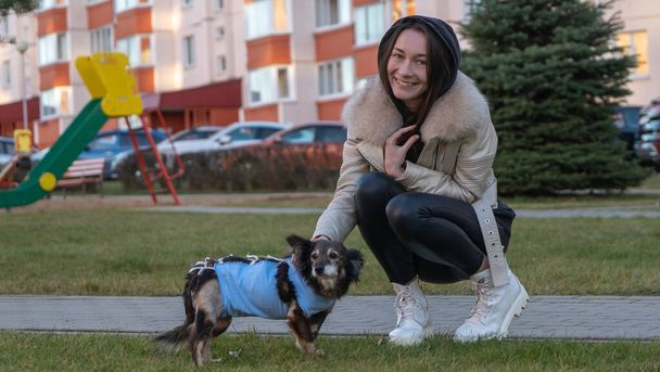A girl walks on the street with a small dog after surgery. The dog is wearing a medical blanket. Animal healthy concepts. Space for text. - Foto, immagini