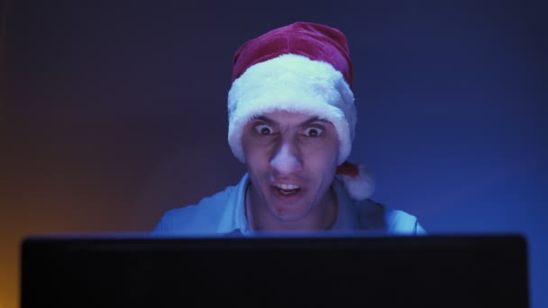 Man in santa claus hat rejoices in winning online game while looking at laptop - Footage, Video