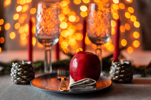 Різдвяний святковий стіл подається з двома келихами, свічками, червоним аплетом на сірій тарілці з натуральною лляною серветкою та виделкою на сяючому гірляндному фоні. атмосфера зимових канікул
. - Фото, зображення