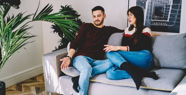 Young spouse in casual wear spending weekend time in home apartment for discussing together pastime and gather bonding, Caucasian boyfriend and girlfriend communicate in modern living room - Foto, afbeelding