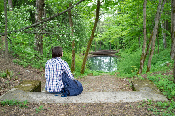Nyugodt nő egy városi hátizsák ül a kőlépcsőn élvezi a gyönyörű táj, tó és erdő, a parkban. - Fotó, kép