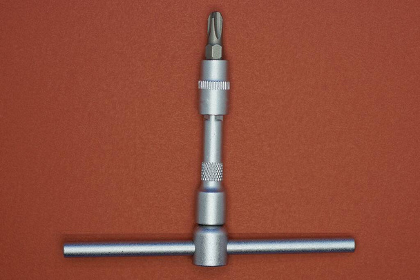 ein Werkzeug aus einem grauen Eisen-Schraubenzieher liegt auf einem braunen Tisch - Foto, Bild