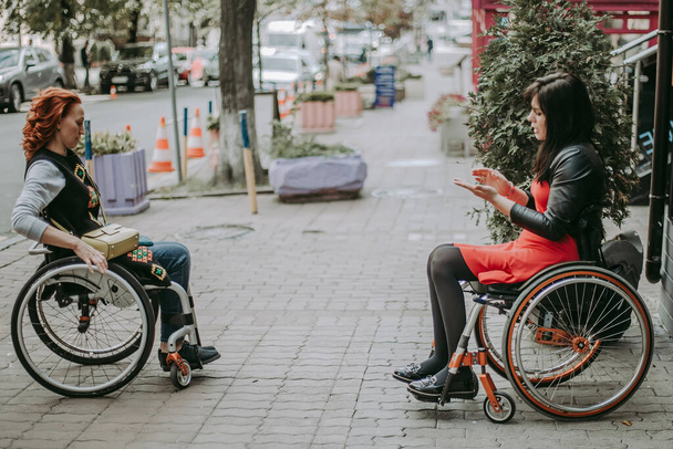 Dos chicas en sillas de ruedas viajan por las calles centrales. Amigos con discapacidad se comunican en las calles de la ciudad. - Foto, Imagen
