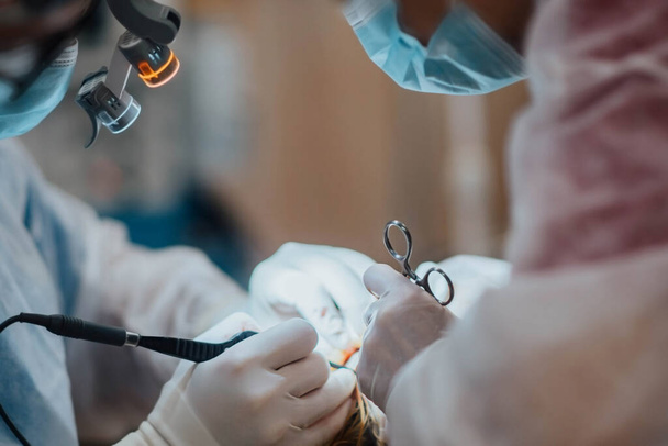 chirurg plastyczny operuje pacjenta w okularach i latarce na sali operacyjnej. - Zdjęcie, obraz