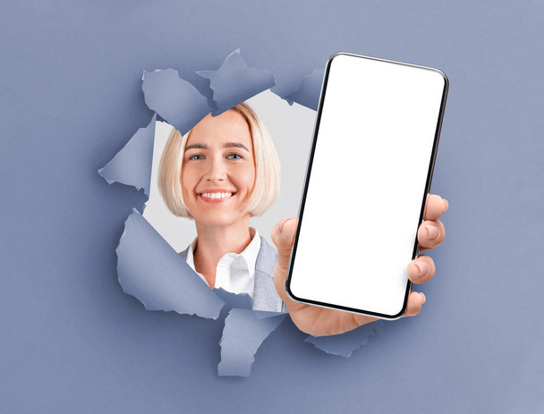 maduro senhora mostrando preto vazio smartphone tela através de rasgado papel - Foto, Imagem