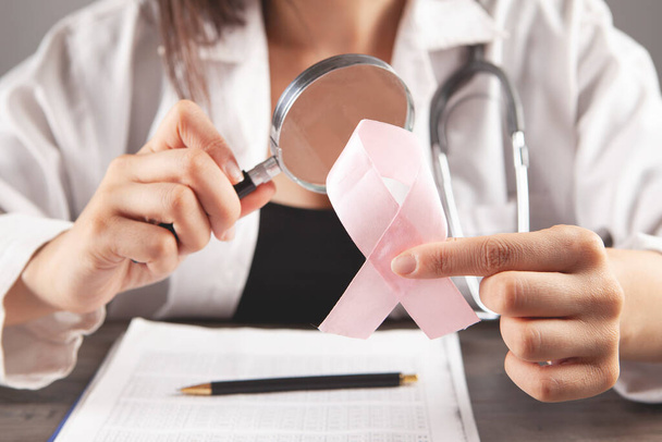 el médico sostiene una lupa y una cinta rosa. concepto de cáncer de mama - Foto, Imagen