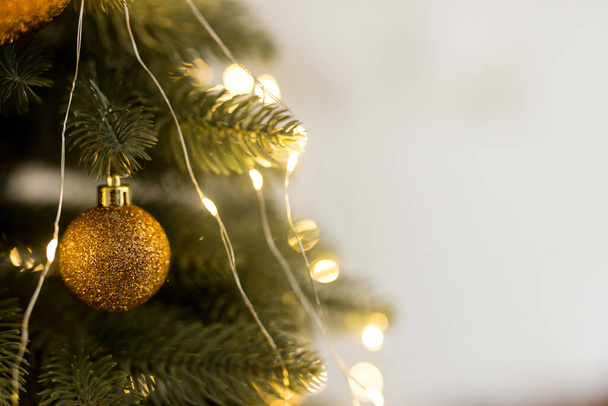 Κοντινό πλάνο του χρυσού παιχνιδιού μπάλα και γιρλάντες σε πράσινο-κίτρινο χριστουγεννιάτικο δέντρο - Φωτογραφία, εικόνα