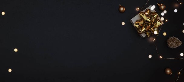 2022 Weiße Geschenkschachtel mit goldenem Band, Neujahrskugeln und funkelnden Lichtergirlanden in weihnachtlicher Komposition auf schwarzem Hintergrund als Grußkarte. Dekoration und Kopierraum für Ihren Text - Foto, Bild