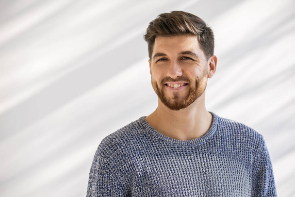 A happy man with one large front tooth instead of two incisors. Dental anomaly with a giant front tooth. Young man with a trendy hairstyle and beard in a gray sweater. Dental pathology in middle age - Photo, Image