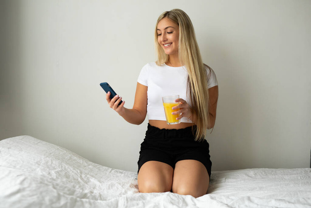 portrait of a beautiful young woman with a glass of juice and a phone - Fotó, kép