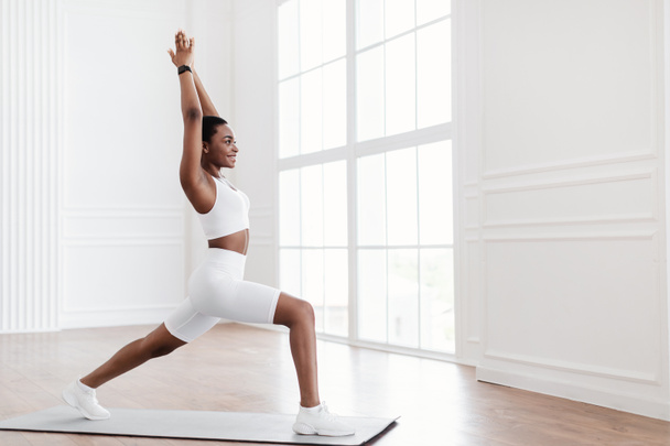 jonge zwart vrouw staande in krijger pose op fitness mat - Foto, afbeelding