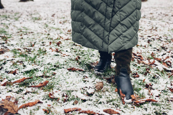 Detailní záběr ženských zimních bot. Žena kráčející ve zasněženém parku v dlouhém teplém kabátu a vysokých zelených semišových botách - Fotografie, Obrázek