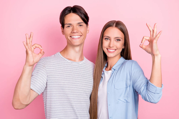 Photo of pretty shiny young lovers dressed casual outfits showing okey signs smiling isolated pink color background - Photo, Image