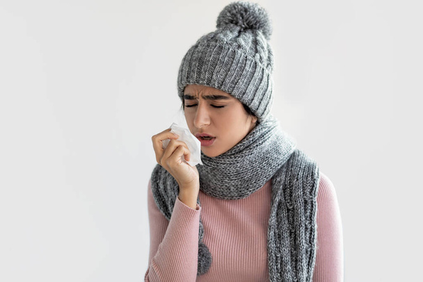 Unhappy millennial indian female in scarf and hat feeling bad, sneezes in napkin suffering from diseases - Фото, зображення