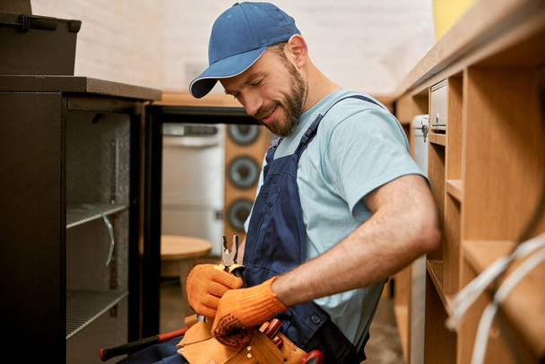 Χαρούμενος επισκευαστής που επιλέγει εργαλείο για την επισκευή ψυγείου - Φωτογραφία, εικόνα