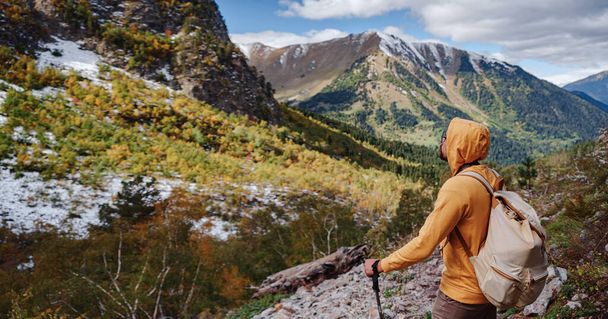 travel to Caucasus mountains in Karachay-Cherkessia, Arkhyz. Man in yellow hipster hoodie hiking in mountains with travel backpack. Wandering lifestyle, adventure concept autumn vacation in wild - Photo, Image