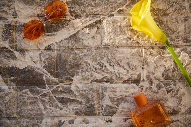 Esthetische stijl van bakstenen achtergrond met oranje parfum flacon en zonnebril. Decoraties van gele calla. Vrouwelijk, vintage concept. Kopieerruimte, trendy schaduwen. - Foto, afbeelding