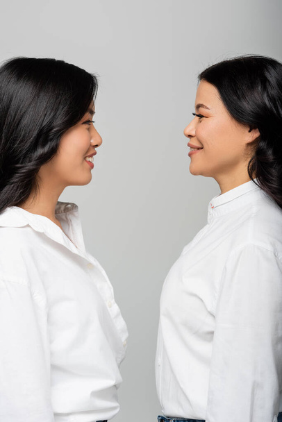 side view of happy asian mother looking at cheerful young adult daughter isolated on grey - Photo, Image