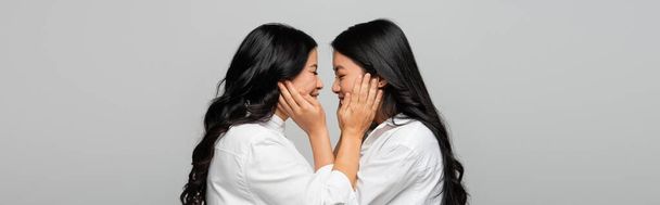 side view of happy asian mother and young adult daughter touching cheeks of each other isolated on grey, banner - Fotó, kép