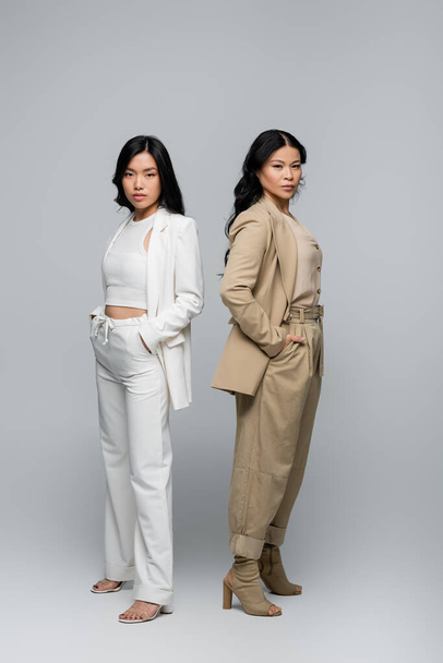 full length of stylish asian mother and young adult daughter in suits posing on grey - Φωτογραφία, εικόνα