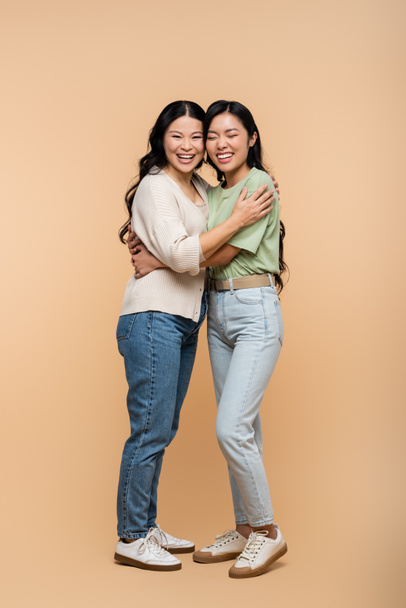 full length of cheerful asian mother hugging young adult daughter on beige  - Photo, Image