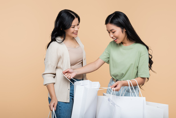 happy asian woman looking at shopping bag near mother isolated on beige - Photo, Image