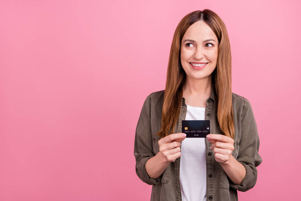 Foto van aantrekkelijke volwassen vrouw vroeg zich af look lege ruimte bankkaart winkel betalen geïsoleerd over roze kleur achtergrond - Foto, afbeelding