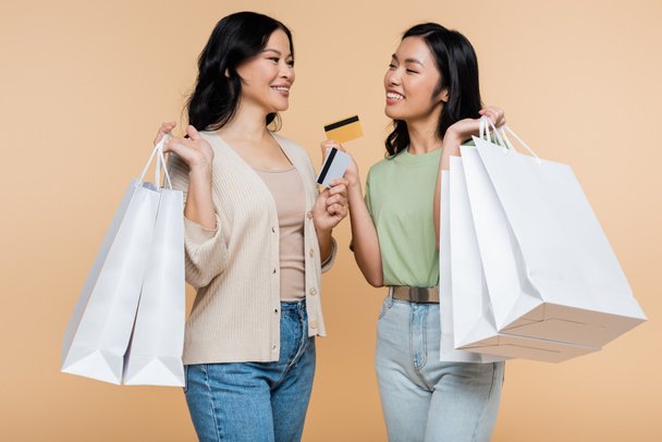 happy asian mother and daughter with shopping bags and credit cards isolated on beige - Photo, Image