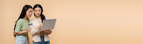 mère asiatique et fille adulte avec carte de crédit regardant ordinateur portable pendant les achats en ligne isolé sur beige, bannière - Photo, image