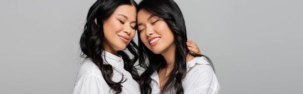 喜びに満ちたアジア系の母親と若い娘白いシャツに身を包んだグレーのバナー - 写真・画像