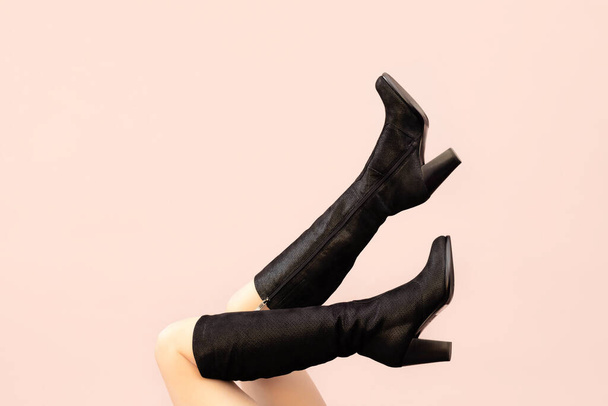 Hermosas piernas de mujer sexy caucásica en ante negro botas delgadas con patrón en tacones sobre fondo beige rosa claro, espacio de copia, vista frontal. Humor sexy - Foto, imagen