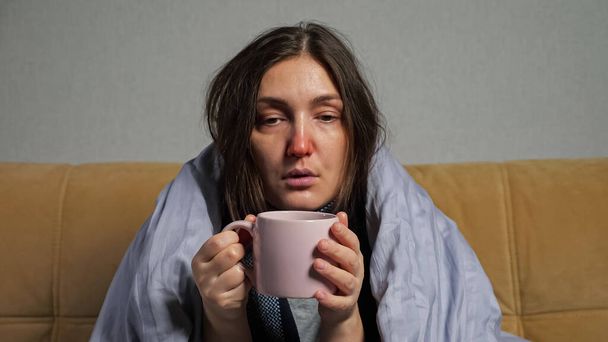 Vrouw ziek en drinkt thee gewikkeld in deken op de bank - Foto, afbeelding