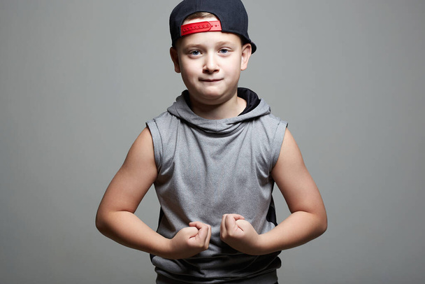 strong Child. Funny Little Boy in Hat. Sport Kid. Young bodybuilder showing his hand biceps muscles - Foto, immagini