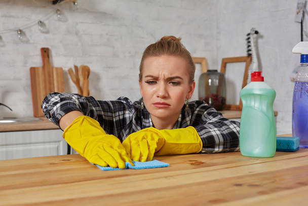 Jovem mulher em luvas de proteção limpa uma mesa na cozinha com um pano - Foto, Imagem