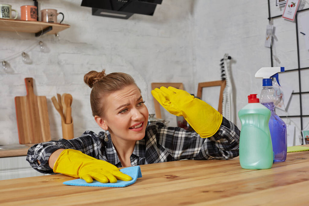 Mujer joven con guantes protectores limpia una mesa en la cocina con un trapo - Foto, Imagen