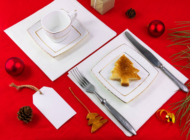 Χριστουγεννιάτικο τραπέζι ρύθμιση τοστ σε λευκό πιάτο ασημικά σε κόκκινο τραπεζομάντιλο φόντο επίπεδη θέσει. Πρωτοχρονιά εορταστική διακόσμηση εστιατόριο δείπνο Χειμερινές διακοπές Ευχετήρια κάρτα mockup πρόσκληση σχεδιασμό - Φωτογραφία, εικόνα