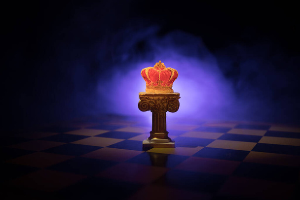 Gyönyörű korona a sakktáblán. sakk társasjáték koncepció üzleti ötletek és a verseny és stratégiai ötletek koncepció. Sakkfigurák sötét háttérrel, füsttel és köddel. Szelektív fókusz - Fotó, kép