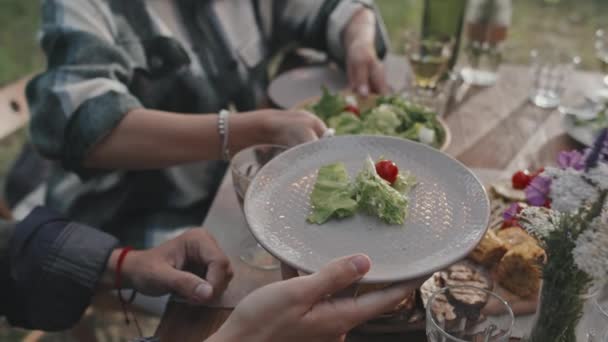 Hitaasti lähikuva tunnistamaton nainen tarjoilee salaattia vieraalleen syödessään illallista ulkona kesäpäivänä - Materiaali, video