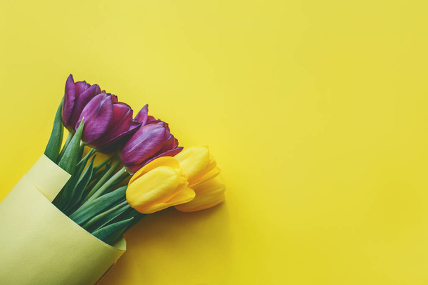 Ramo de hermosos tulipanes morados y amarillos sobre fondo amarillo, vista superior. - Foto, imagen