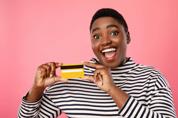 Izgatott afro-amerikai nő mutatja hitelkártya felett rózsaszín háttér - Fotó, kép