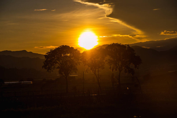 A sunset sky over the mountains and trees - 写真・画像