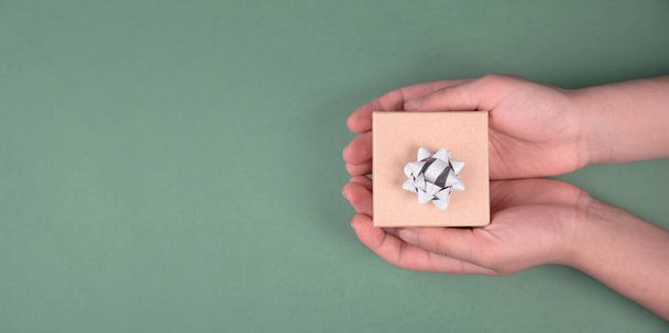 Holding a small gift box in the hands on a green colored background, holidays like birthday, fathers day, christmas, copy space for text - Φωτογραφία, εικόνα