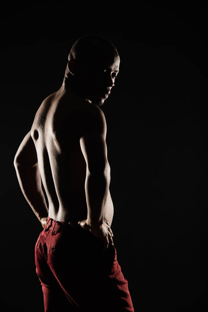 Silhouette of black male is posing in red jeans while looking down - Foto, imagen