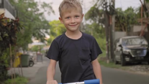 Plan de suivi de 7 ans garçon caucasien équitation scooter à l'extérieur en Indonésie - Séquence, vidéo