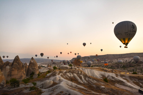 カッパドキアの奇妙な山々の間で日の出に舞い上がる驚くべき気球 - 写真・画像